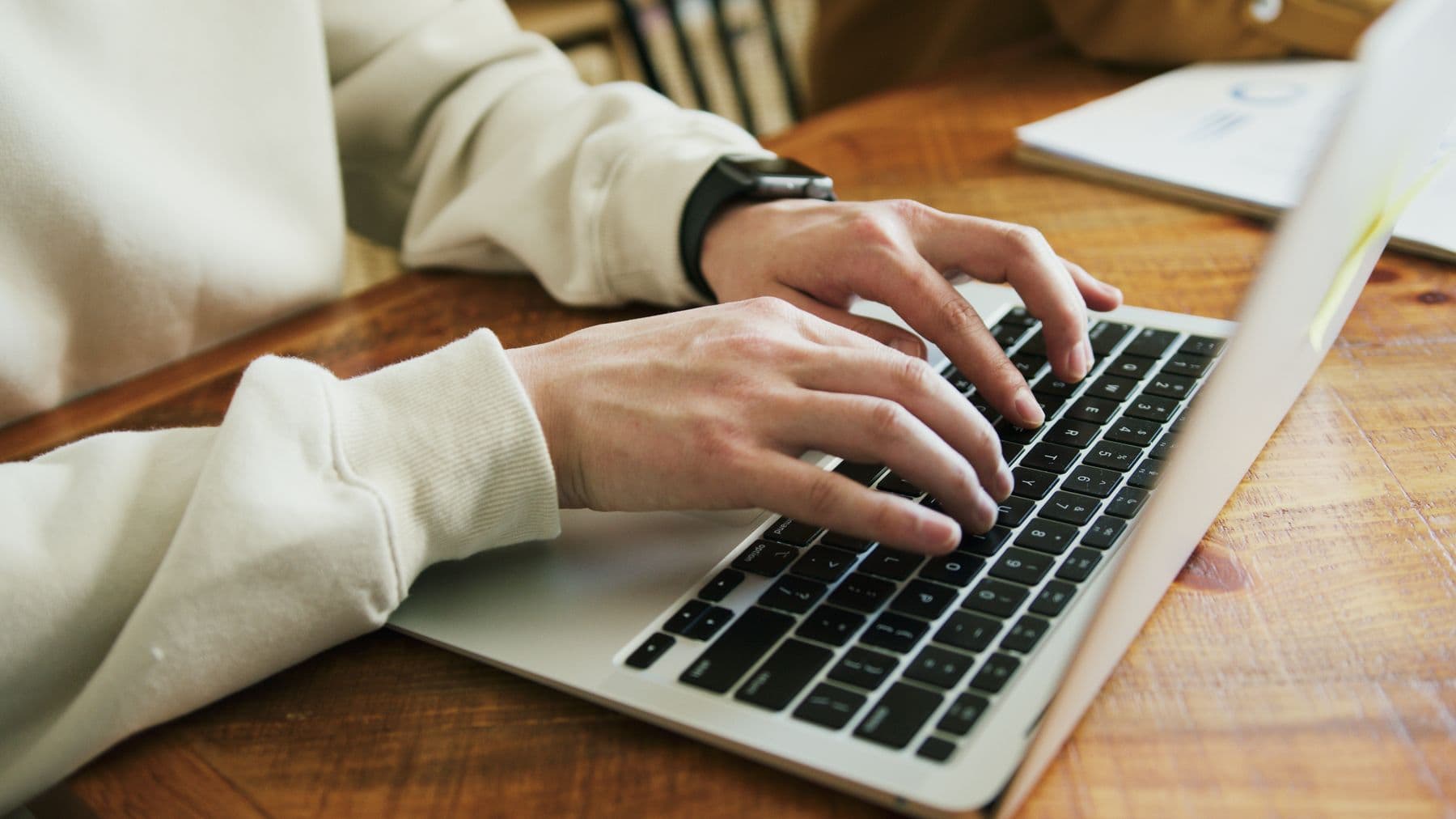 Close-up of hands typing on a laptop with a report in soft focus behind